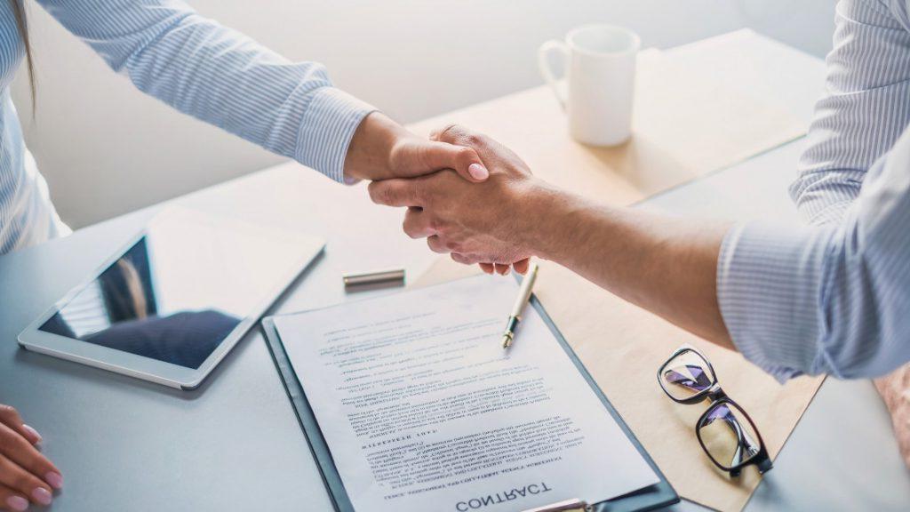 Two people shaking hands over an employment contract